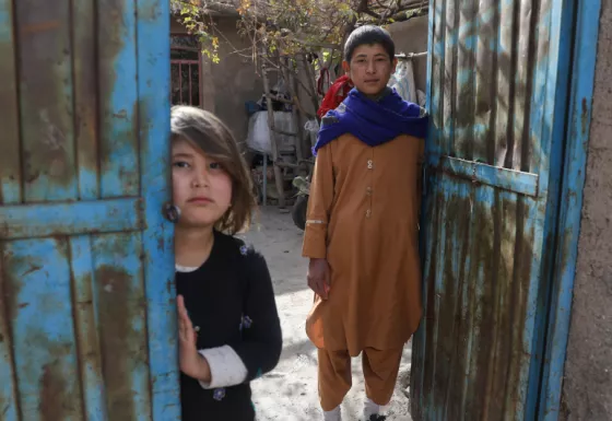 Participant Hassan and his little sister stand outside their home in Afghanistan.