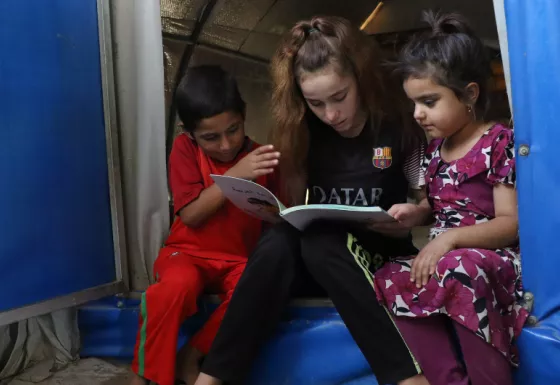 Participant Nadia reads to her siblings at their home in a displacement camp in Iraq.