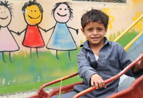 Participant sits on a slide outside a War Child child-friendly space in Yemen.