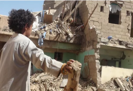 A boy in Yemen standing in front of a destroyed building. 