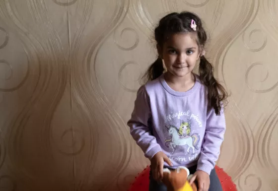 Miriam is wearing a purple unicorn jumper and is posing against a wall