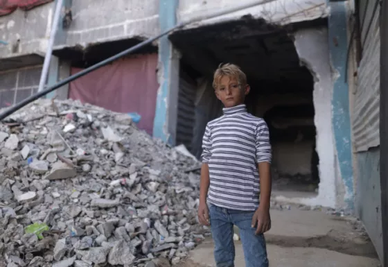 A boy standing next to a collapsed building in Gaza.