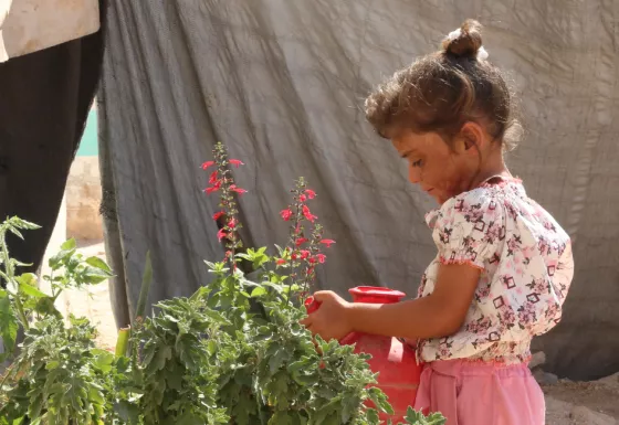 Sama watering flowers in a refugee camp in Syria.