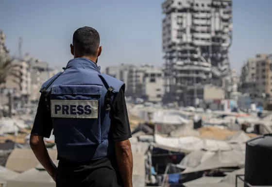 A member of the press standing wearing a press vest looking out to Gaza.