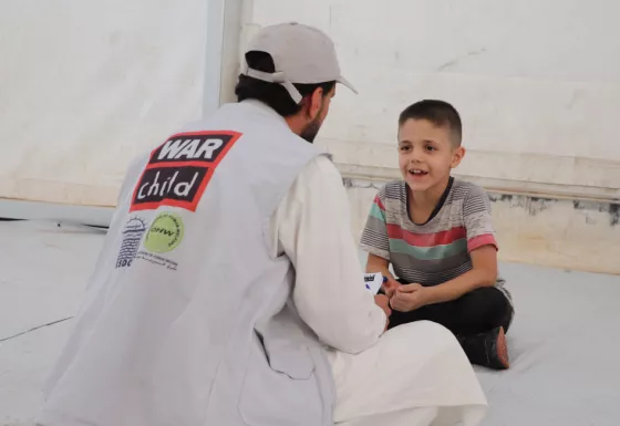 Afghan boy sat legs crossed speaking with a War Child staff.