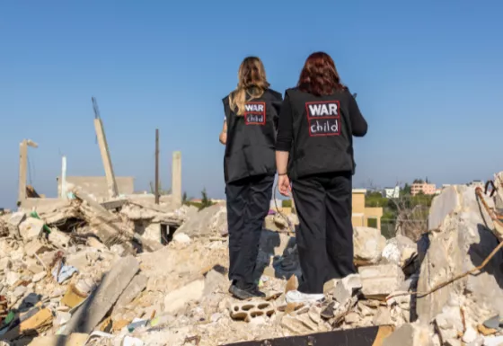 Two members of War Child staff standing on rubble