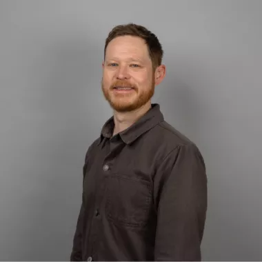 A man standing and smiling in front of a grey background.