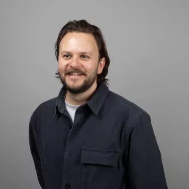 A man standing and smiling in front of a grey background.