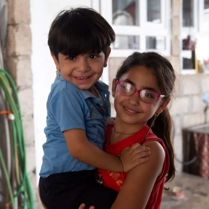 Participant Soleen carries her younger brother in their home.