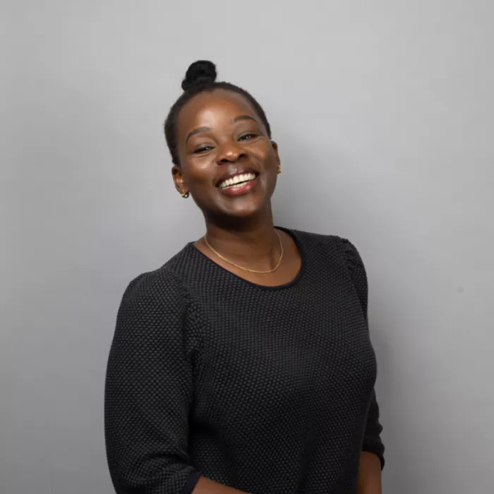 A woman standing and smiling in front of a grey background.