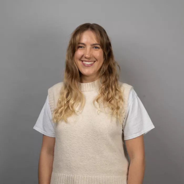 A girl standing and smiling in front of a grey background.