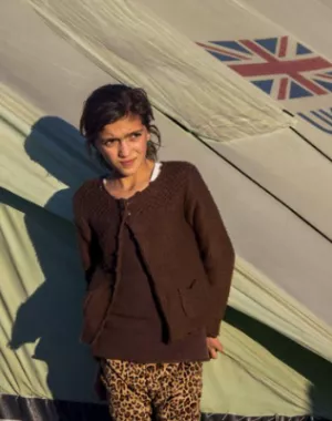 Girl in front of a tent bearing the UK Aid logo in a displacement camp.