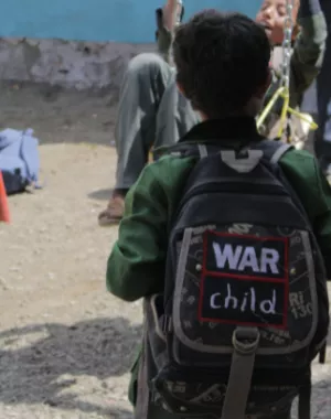 Child in Yemen wears a War Child rucksack outside their school.