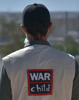 War Child staff member stands with back to camera showing jacket with War Child logo on their back.