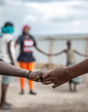 Children stand in a circle holding hands as they play games at a War Child child-friendly space in the DRC.