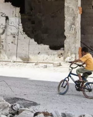 Syrian boy cycles around the city which has been destroyed by conflict.
